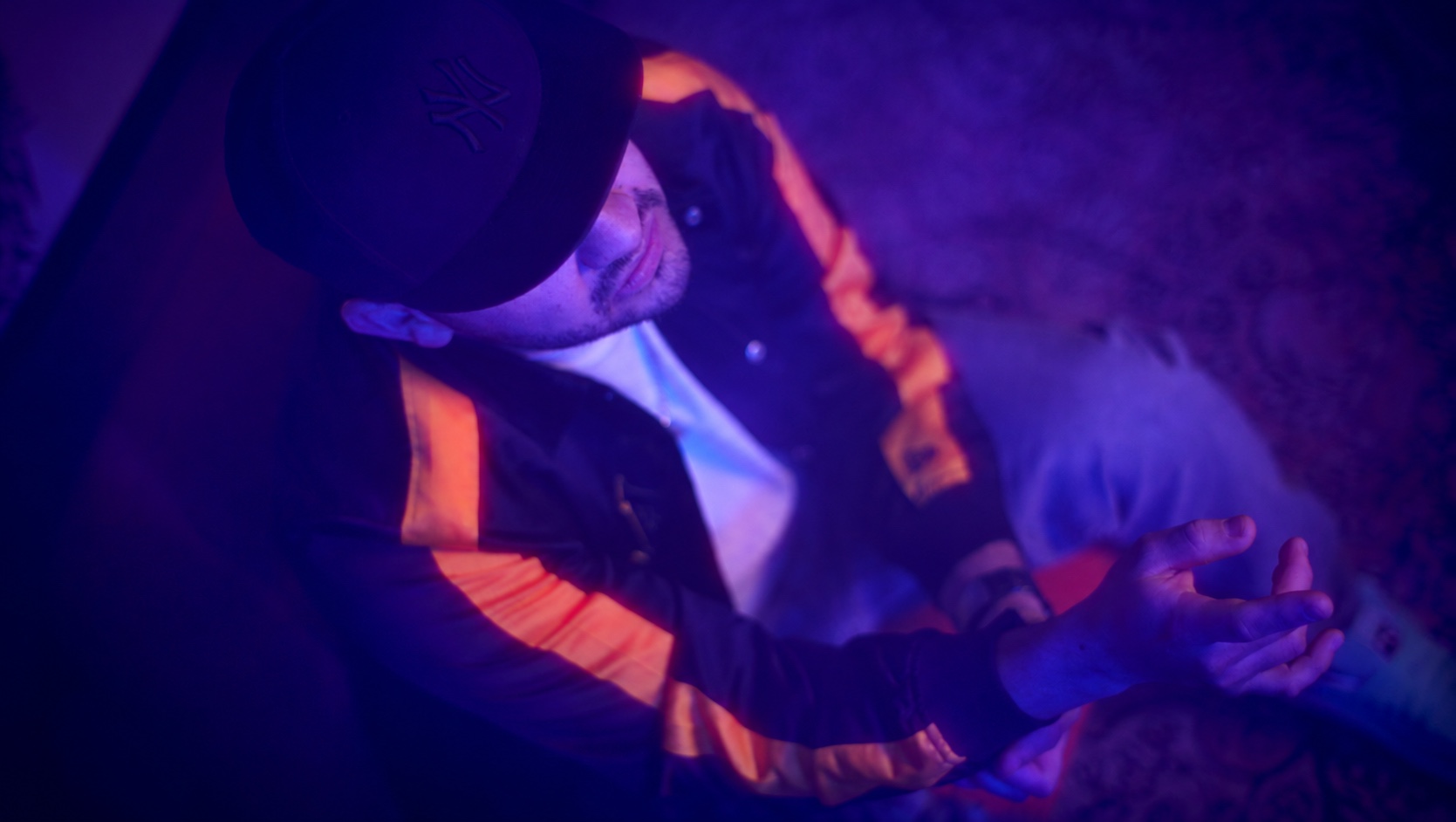 Filmstill von oben: Künstler mit Kappe und bewegten Händen im violetten Licht